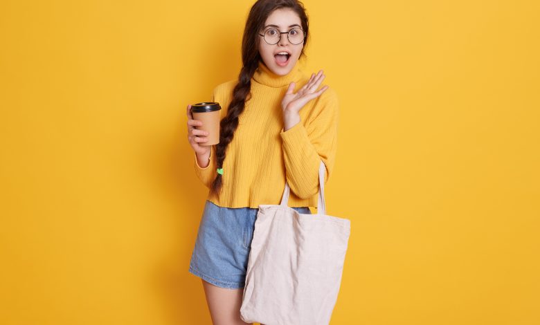 #PraCegoVer: Imagem uma mulher segurando uma sacola de compras e um copo na mão.