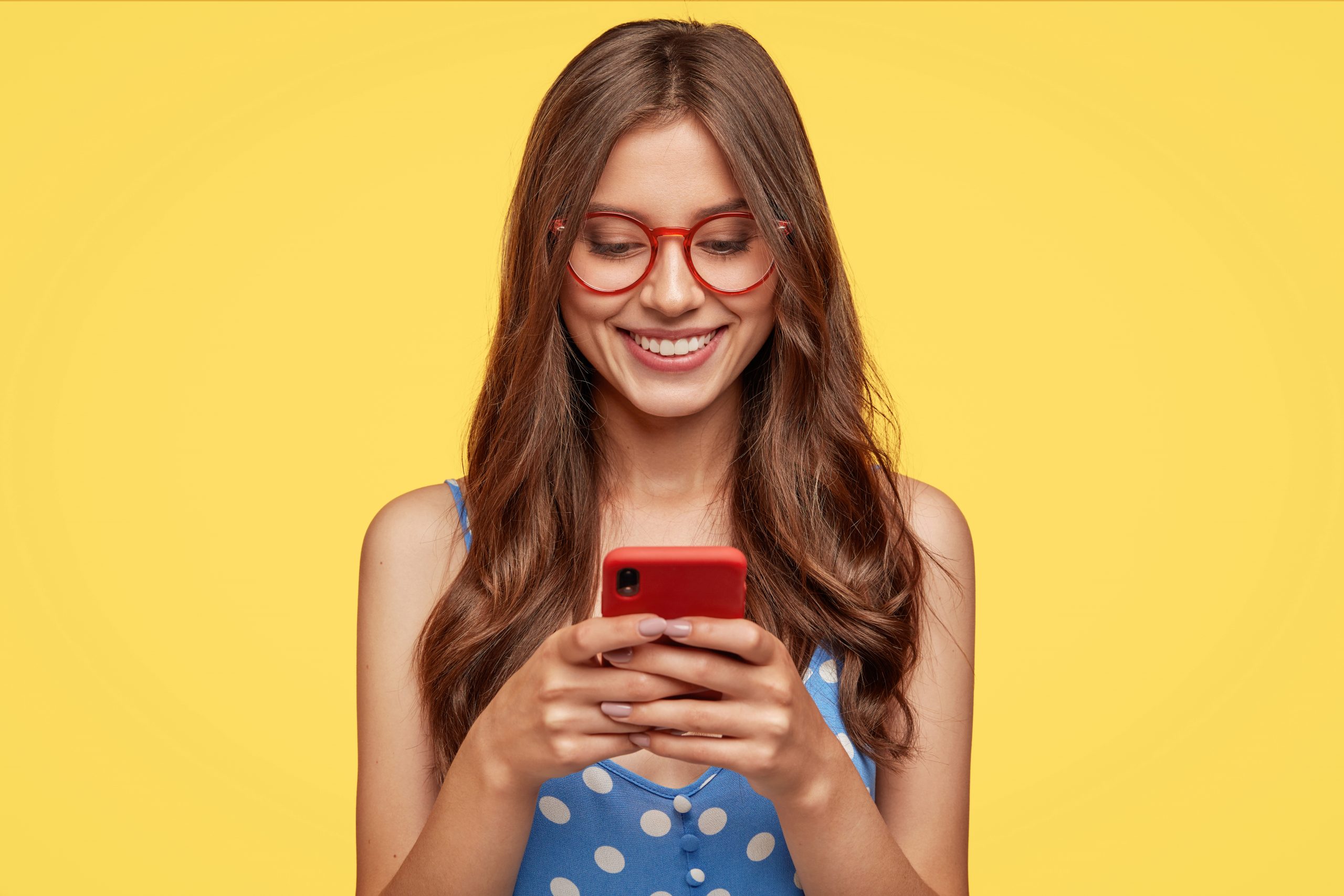 #PraCegoVer: Imagem de uma mulher olhando no celular com um fundo amarelo.