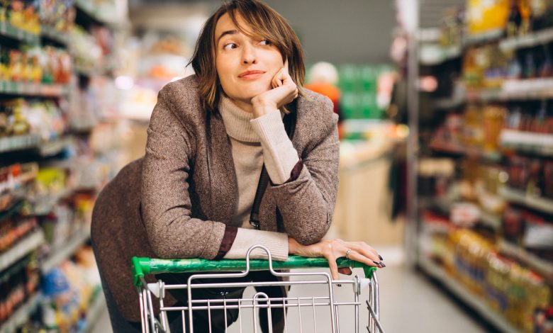 #PraCegoVer: Imagem de uma mulher pensativa com um carinho de compras no supermercado.