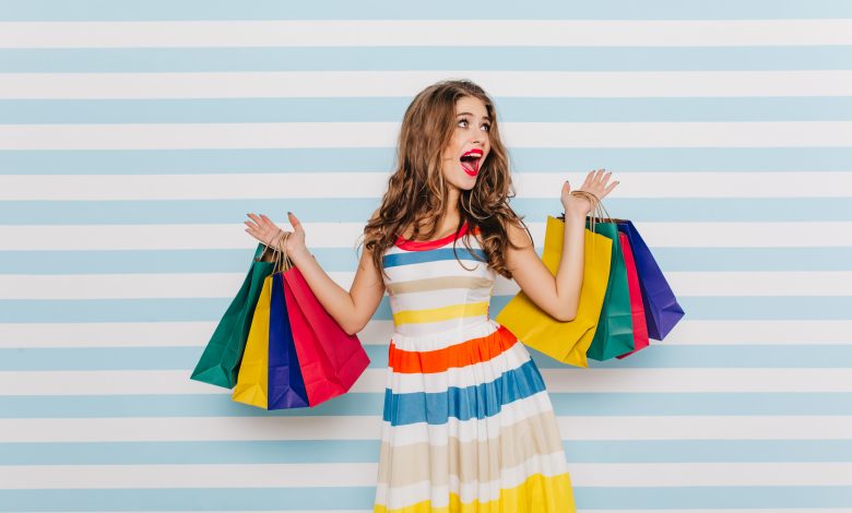 #PraCegoVer: Imagem de uma mulher segurando sacolas de compras e emocionada.