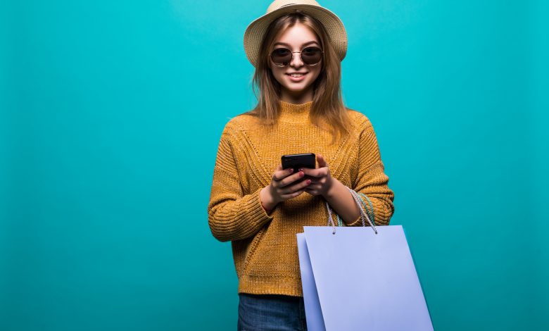 #PraCegoVer: Imagem de uma mulher com uma sacola de compras e utilizando o celular.