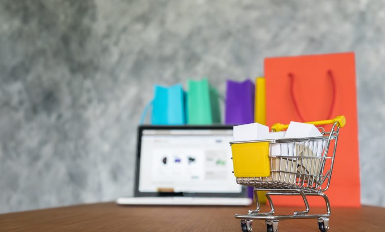 #PraCegoVer: Imagem de um mini carinho de supermercado com compras e um computador ao fundo.