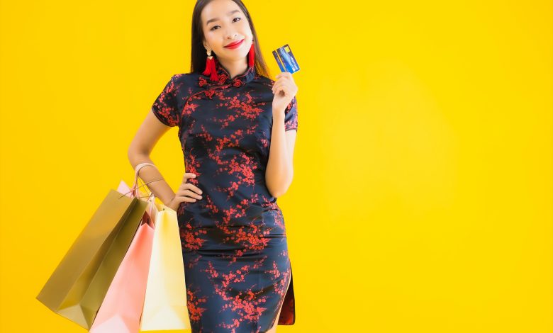 #PraCegoVer: Mulher Japonesa segurando sacolas de compras e um cartão de crédito