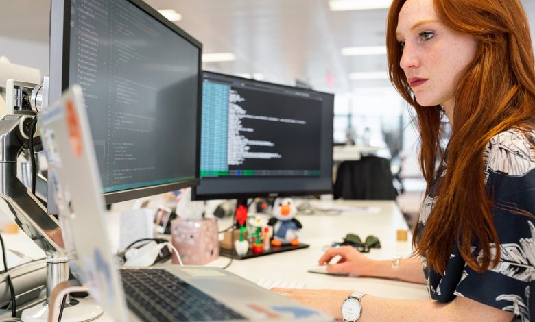 #PraCegoVer: Imagem de uma mulher em frente a um computador em uma estação de trabalho.