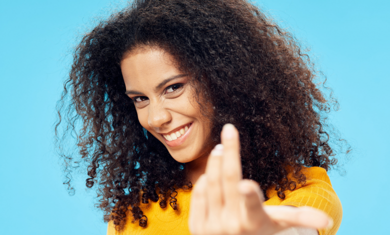 #PraCegoVer: Imagem de uma mulher sorrindo com uma camiseta amarela em um fundo azul. - Fonte Imagem - Canva Pro