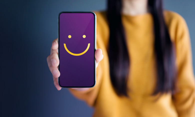#PraCegoVer: Imagem de uma mulher segurando um telefone com um rosto feliz.