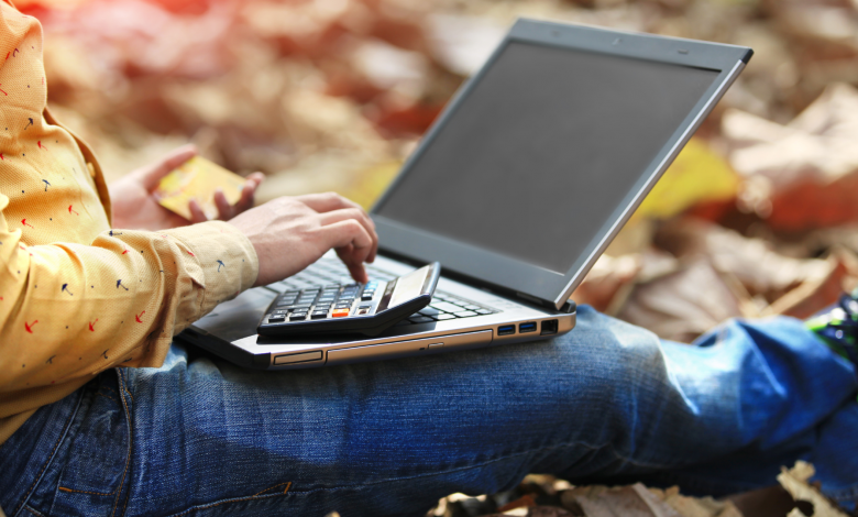 #PraCegoVer: Imagem de uma pessoa com um computador no colo com uma calculadora e um cartão de crédito. - Imagem Divulgação: Canva Pro