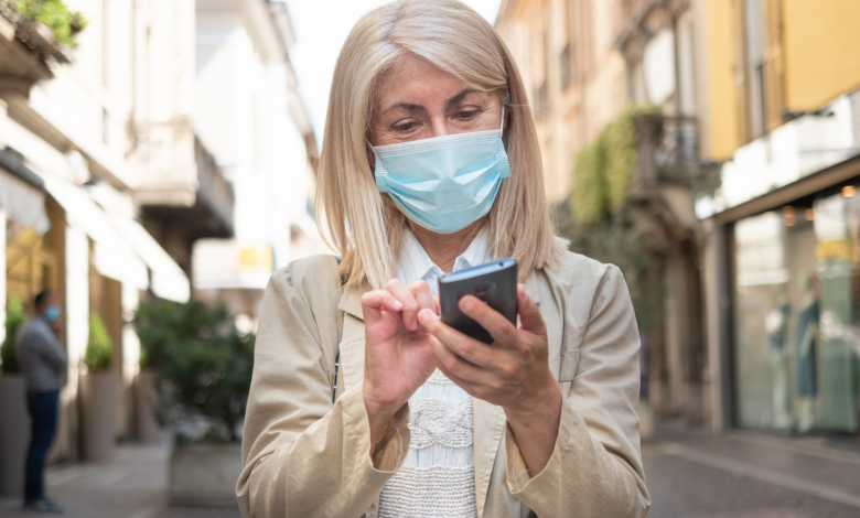 #PraCegoVer: Imagem de uma mulher de mascara no rosto em proteção ao Covid-19 e com o celular em mãos. - Imagem Divulgação: Canva Pro